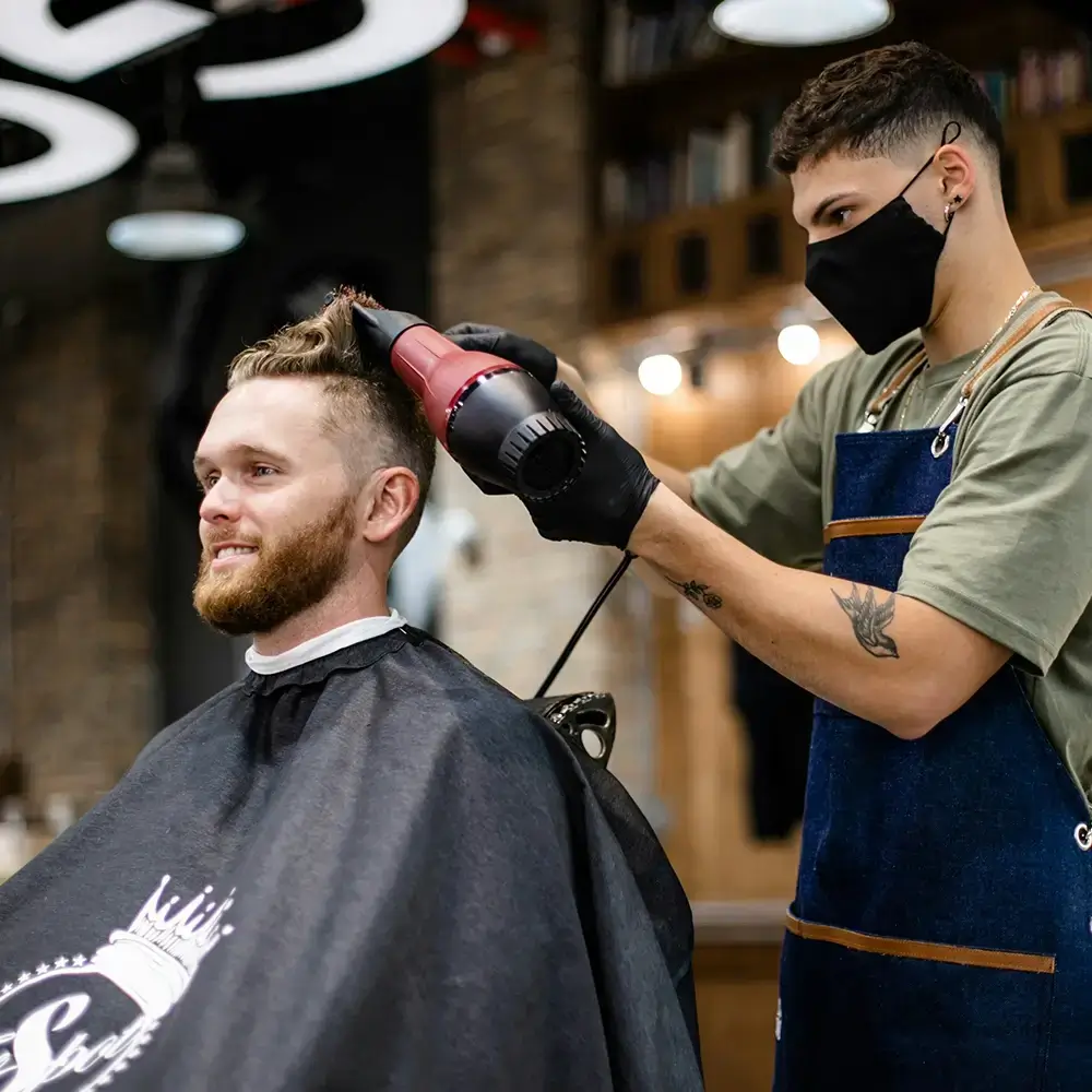 Barber styling a client’s hair with a blow dryer inside a modern salon.