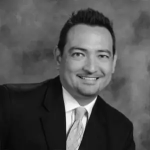 Black-and-white professional portrait of Bruce Dye wearing a suit and tie against a studio-style background.