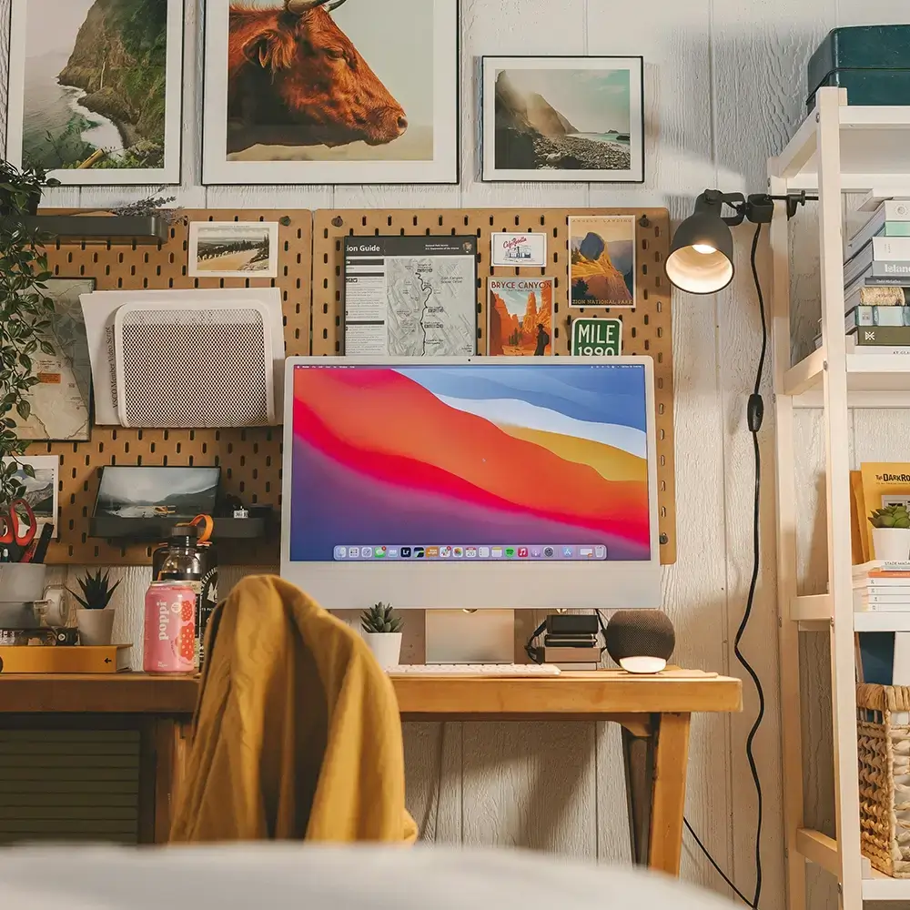 Creative home office with desktop computer, organized pegboard, framed artwork, plants, and desk accessories.