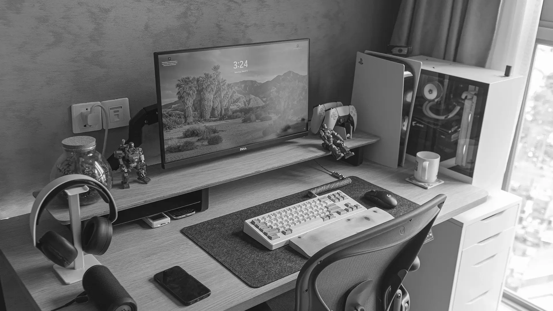 Monochrome home workstation with ultrawide monitor, mechanical keyboard, headphones, desktop PC, PlayStation 5, controller, and organized desk accessories.