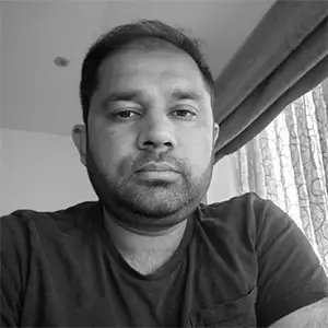 Black-and-white casual portrait of Muhammad Ijaz Munir seated indoors beside a window.
