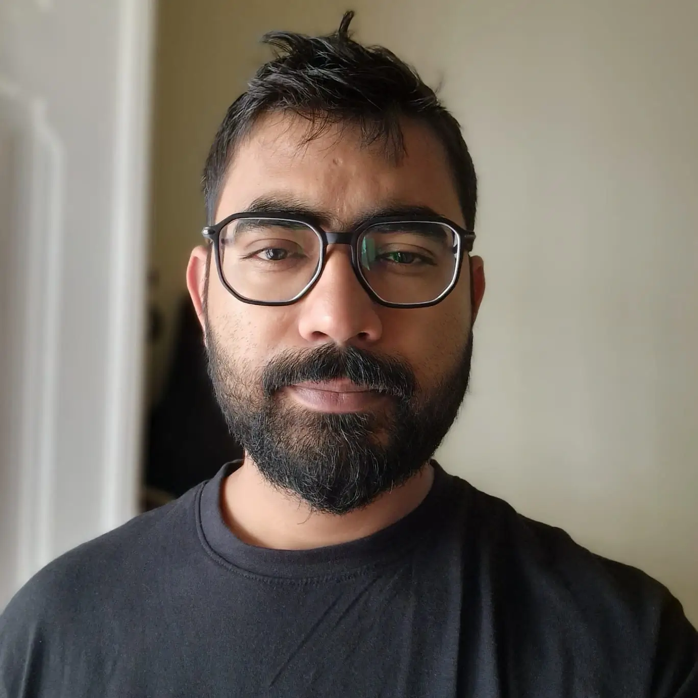 Professional portrait of Muhammad Saad wearing black glasses and a dark shirt against a softly lit neutral background.