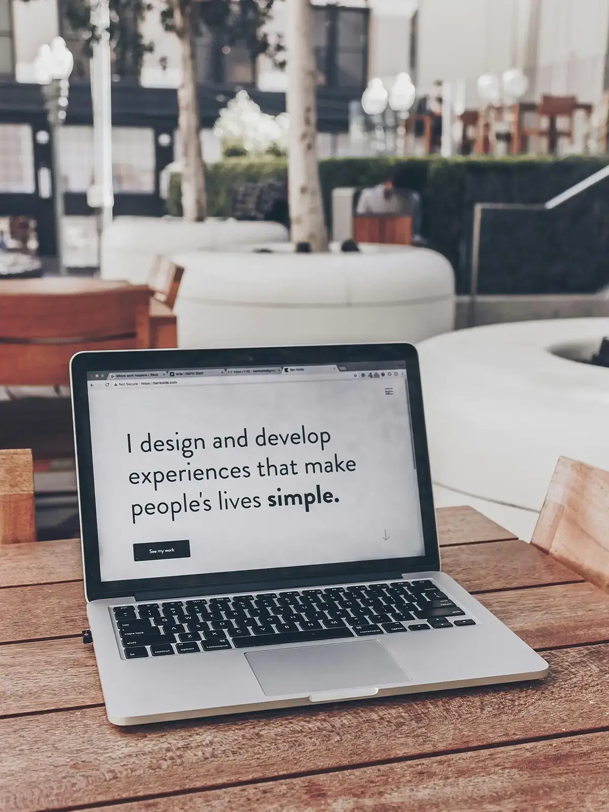 Laptop displaying a minimalist website design on a wooden table in a bright modern workspace.